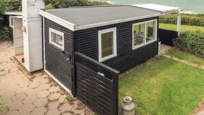 A small, dark-colored house with a flat roof, large windows, and a view of the sea.