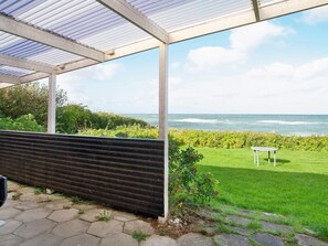 A covered patio with a view of the sea, a grassy area, and a small table.