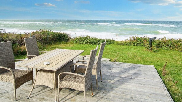 A deck with wicker furniture overlooking the ocean.