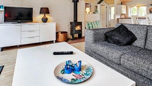 A cozy living room with a fireplace, white brick walls, a sofa, and a flat-screen TV. - 4 Person Holiday Home in Hurup Thy-by Traum (Hurup Thy)
