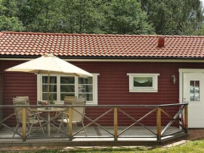 A red building with a tiled roof, a covered patio with chairs and an umbrella, and a white door. - 4 Person Holiday Home in Kyrkhult (Kyrkhult)