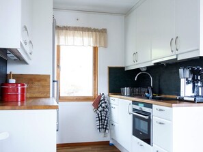A compact kitchen with white cabinets, a wooden countertop, a built-in oven, and a window with a curtain.