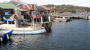 A harbor with a fishing boat docked, a wooden pier, and buildings in the background. - 4 Person Holiday Home in Nordkoster (Stromstad)