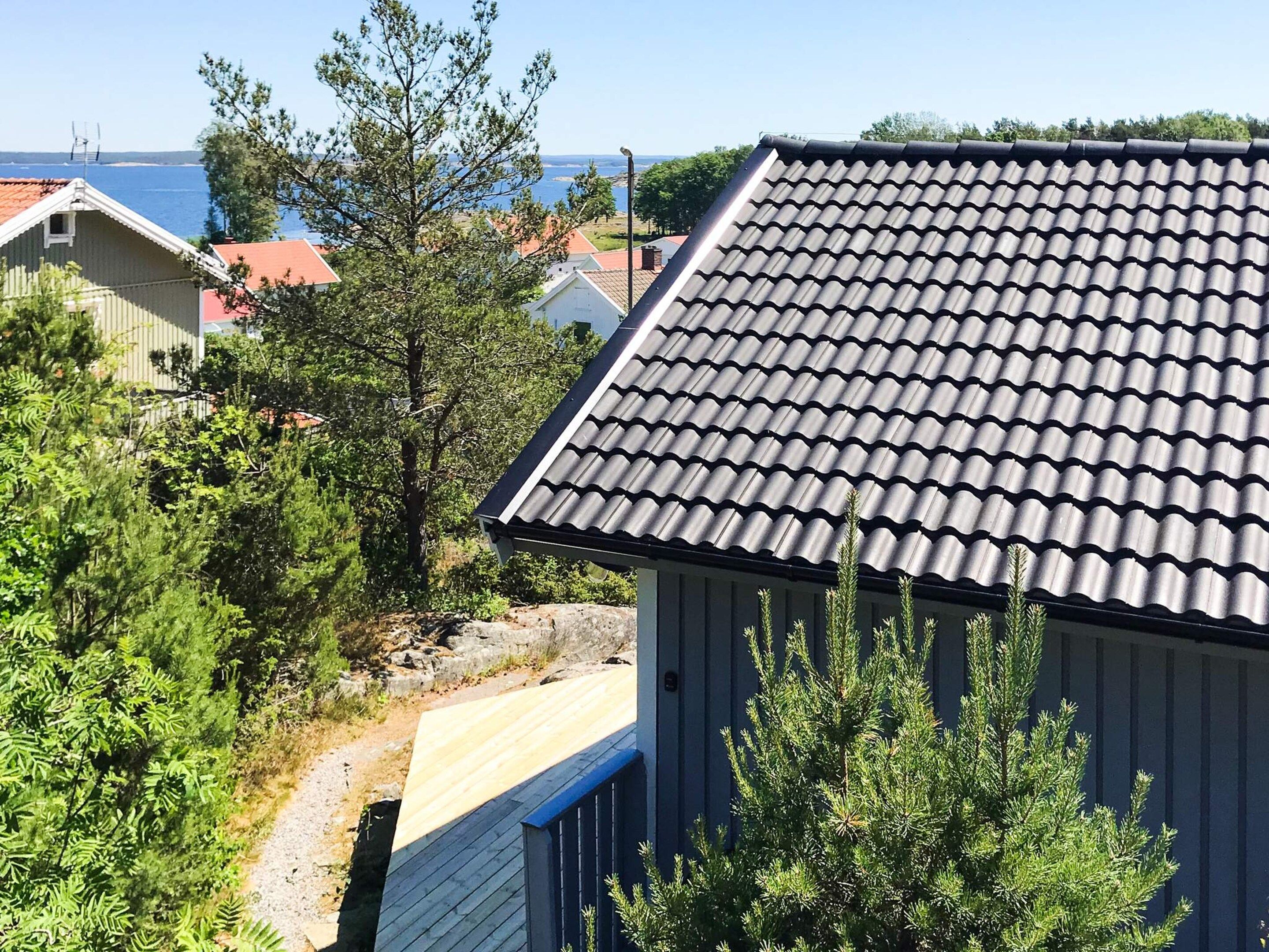 Zona residencial com uma casa de telhado apaleçada, rodeada por vegetação e uma vista desimpedida do mar.
