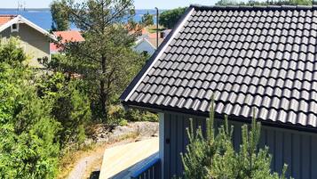 Zona residencial com uma casa de telhado apaleçada, rodeada por vegetação e uma vista desimpedida do mar.