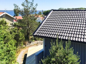 A residential area with a house featuring a tiled roof, surrounded by greenery and a clear view of the sea.