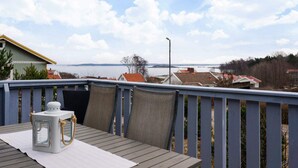 A wooden deck with a table and chairs, overlooking a body of water and houses. - 4 Person Holiday Home in Nordkoster (Stromstad)