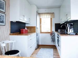 A compact kitchen with white cabinets, a wooden countertop, a window with a valance, a coffee machine, and a black rug. - 4 Person Holiday Home in Nordkoster (Stromstad)