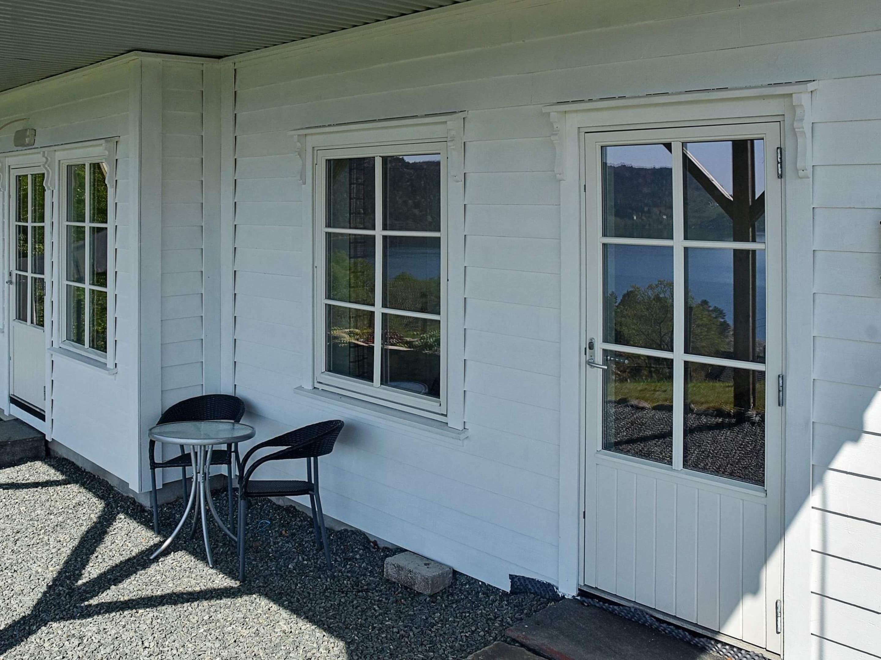 A white building with two doors and windows, a small table, and chairs outside.