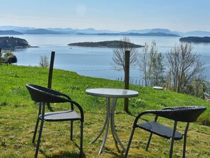 A grassy outdoor seating area with two metal chairs and a small round table, overlooking a lake with distant mountains. - 4 Star Holiday Home in Onarheim (Tysnes)