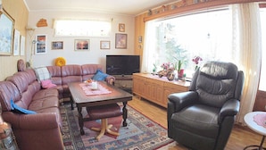A living room with a sectional sofa, a leather armchair, a coffee table, a television, and a large window with curtains.