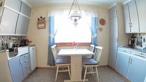 A kitchen with a dining table, chairs, cabinets, and a window with curtains.
