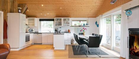 A modern kitchen with white cabinets, a dining area with a table and chairs, and a fireplace.