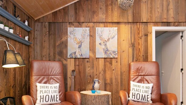 A room with wooden walls, two leather armchairs with pillows, a small round table, and a guitar.