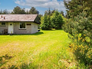 Una casa a un piano con tetto in tegole, un piccolo portico con una panchina e un prato curato.