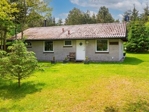 Une maison de plain-pied avec un toit en tuiles, une porte d’entrée et un petit porche doté d’un banc.