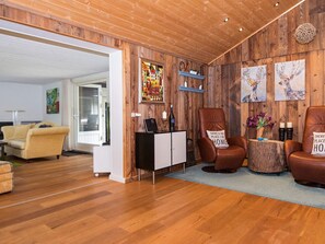 A cozy living room with wooden walls, a sofa, two leather armchairs, a coffee table, and artwork.