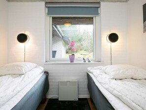 Une chambre avec deux lits, une fenêtre donnant sur l’extérieur, un radiateur et deux lampes fixées au mur.