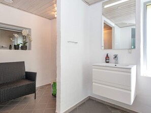 A bathroom with a white vanity, a mirror, and a wicker chair. - 4 Star Holiday Home in Knebel (Knebel)