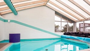 An indoor swimming pool with a clear view of the sky through large windows, a wooden ceiling, and a seating area with cushions. - 4 Star Holiday Home in Knebel (Knebel)