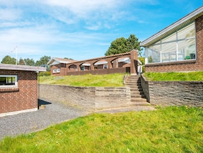A brick building with a staircase leading to a covered area, surrounded by grass and a stone wall.