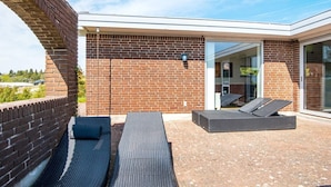 A modern outdoor patio with brick walls, a glass door entrance, and two dark wicker lounge chairs. - 4 Star Holiday Home in Knebel (Knebel)