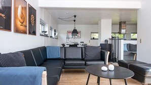 A modern living room with a sectional sofa, a round coffee table, and a kitchen area in the background. - 4 Star Holiday Home in Knebel (Knebel)