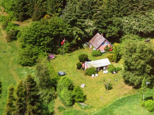 A small house surrounded by dense forest, with a flagpole and a shed nearby. - 6 Person Holiday Home in Braedstrup (Braedstrup)