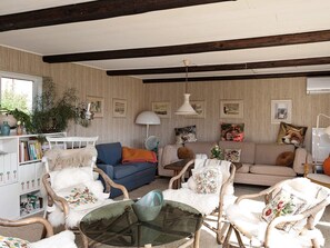 A cozy living room with a high ceiling, striped wallpaper, and a variety of seating including a blue sofa, white armchairs, and a wicker chair. - 6 Person Holiday Home in Braedstrup (Braedstrup)