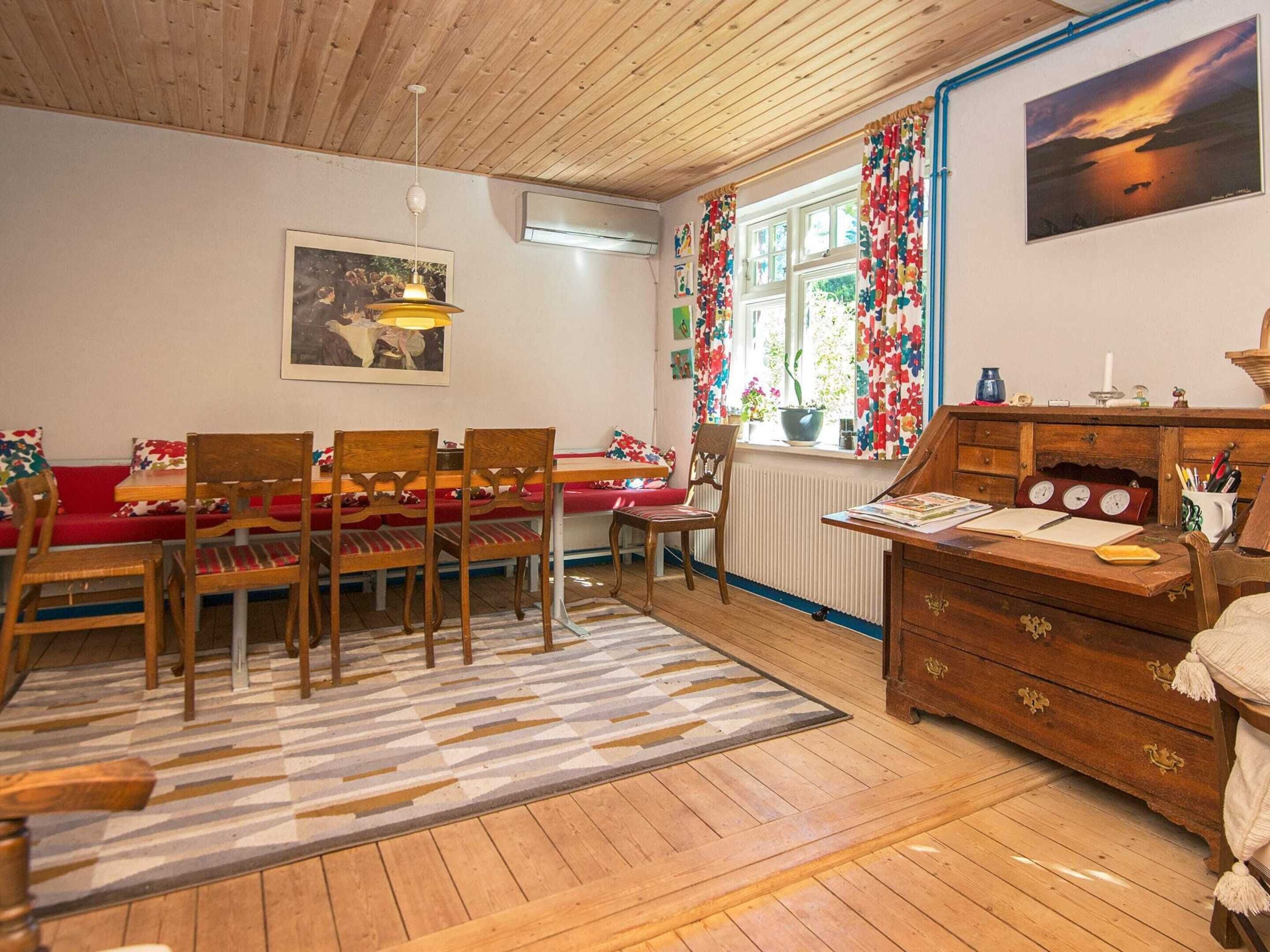 A cozy room with a wooden ceiling, a dining table with chairs, a sofa, a radiator, and a dresser with drawers.