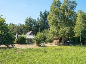 A rustic cabin with a metal roof, surrounded by dense trees and a grassy field. - 6 Person Holiday Home in Braedstrup (Braedstrup)