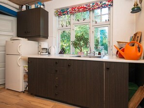 A kitchen with a dark wooden cabinet, a white refrigerator, a coffee maker, and a window with a colorful curtain. - 6 Person Holiday Home in Braedstrup (Braedstrup)