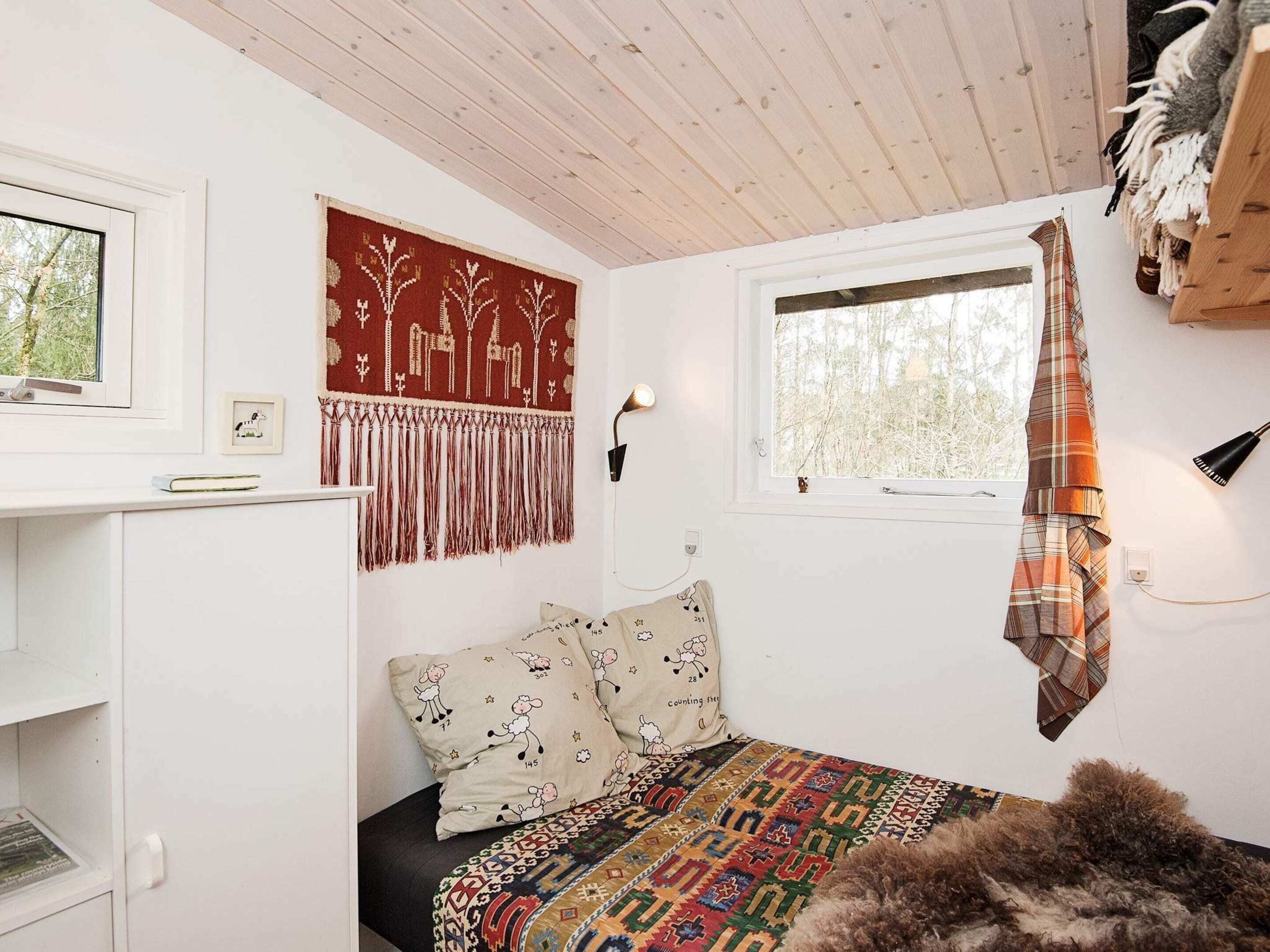 Une chambre confortable avec un lit, une fenêtre, une lampe fixée au mur et un tapis à motifs.