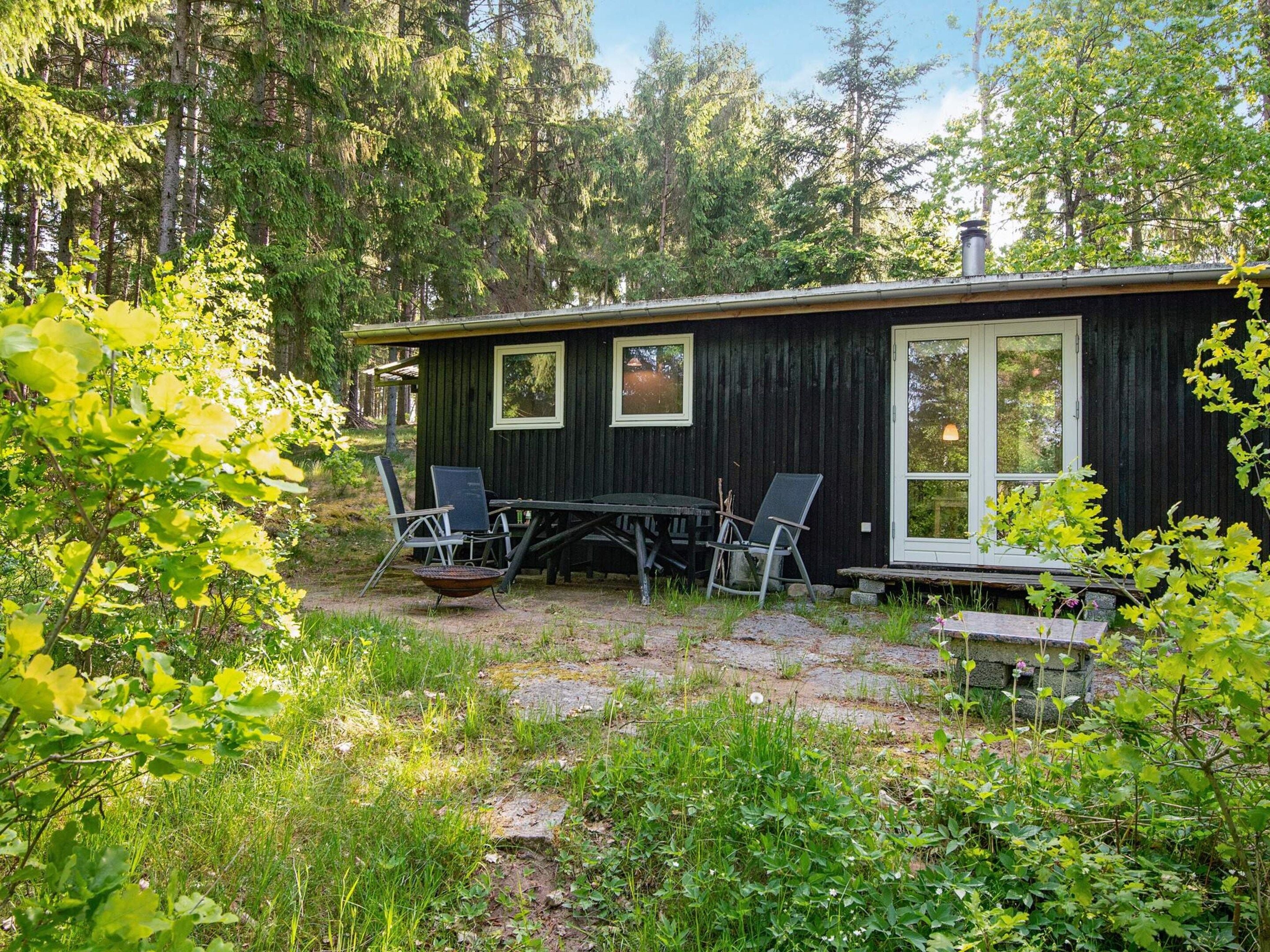 En stuga med ett matbord och stolar, omgiven av grönska och träd.