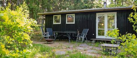 En stuga med ett matbord och stolar, omgiven av grönska och träd.