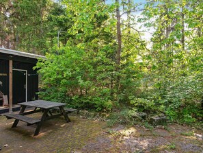 A rustic wooden cabin with a picnic table in a forested area.