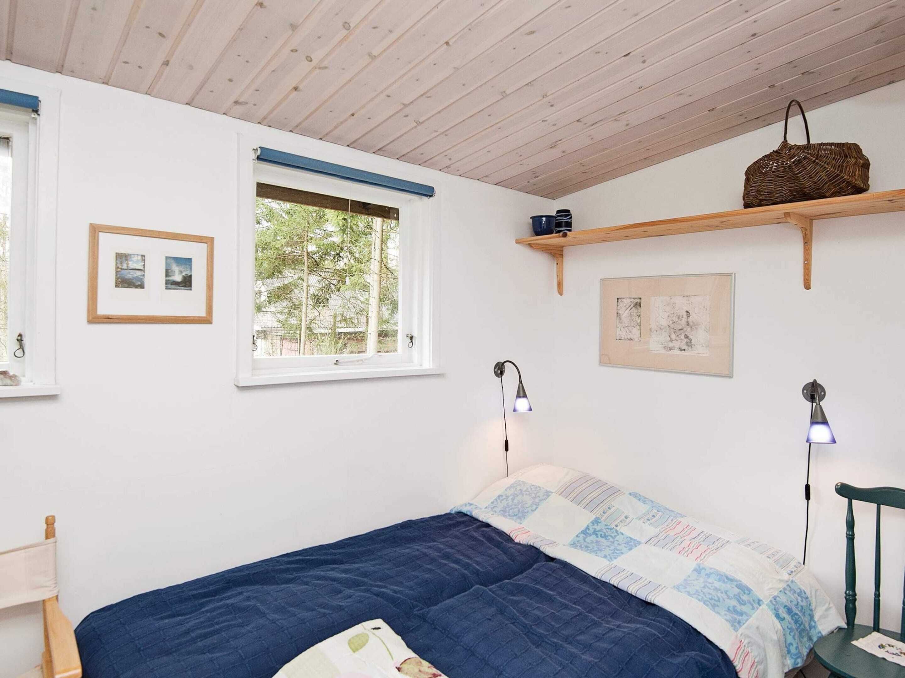 A bedroom with a bed, a window, a shelf with a basket, and two wall-mounted lamps.