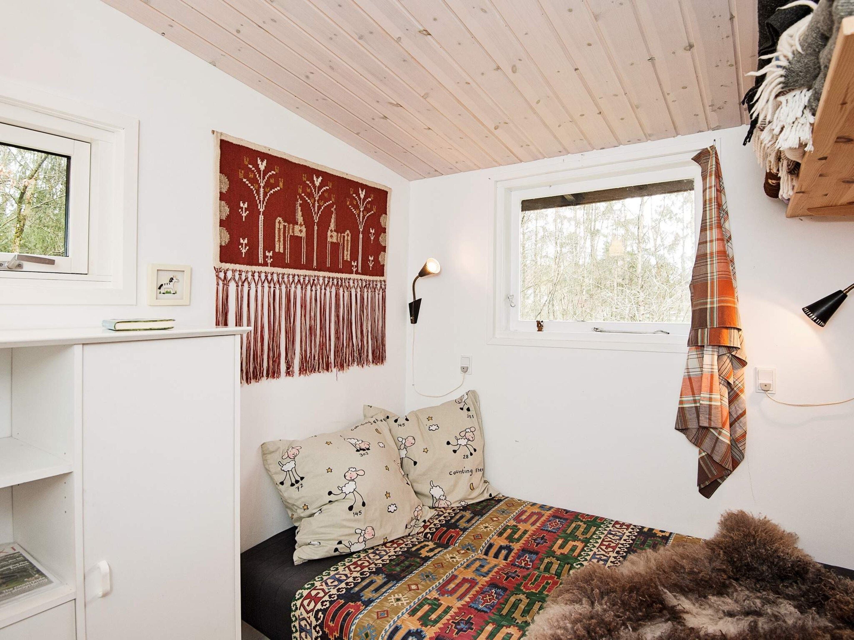 Una habitación con una cama, una ventana, una lámpara de pared y un tapiz.