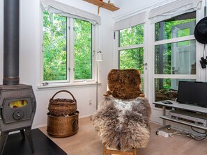 A room with a fireplace, a large window with a view of greenery, a television, and a small table with a basket.