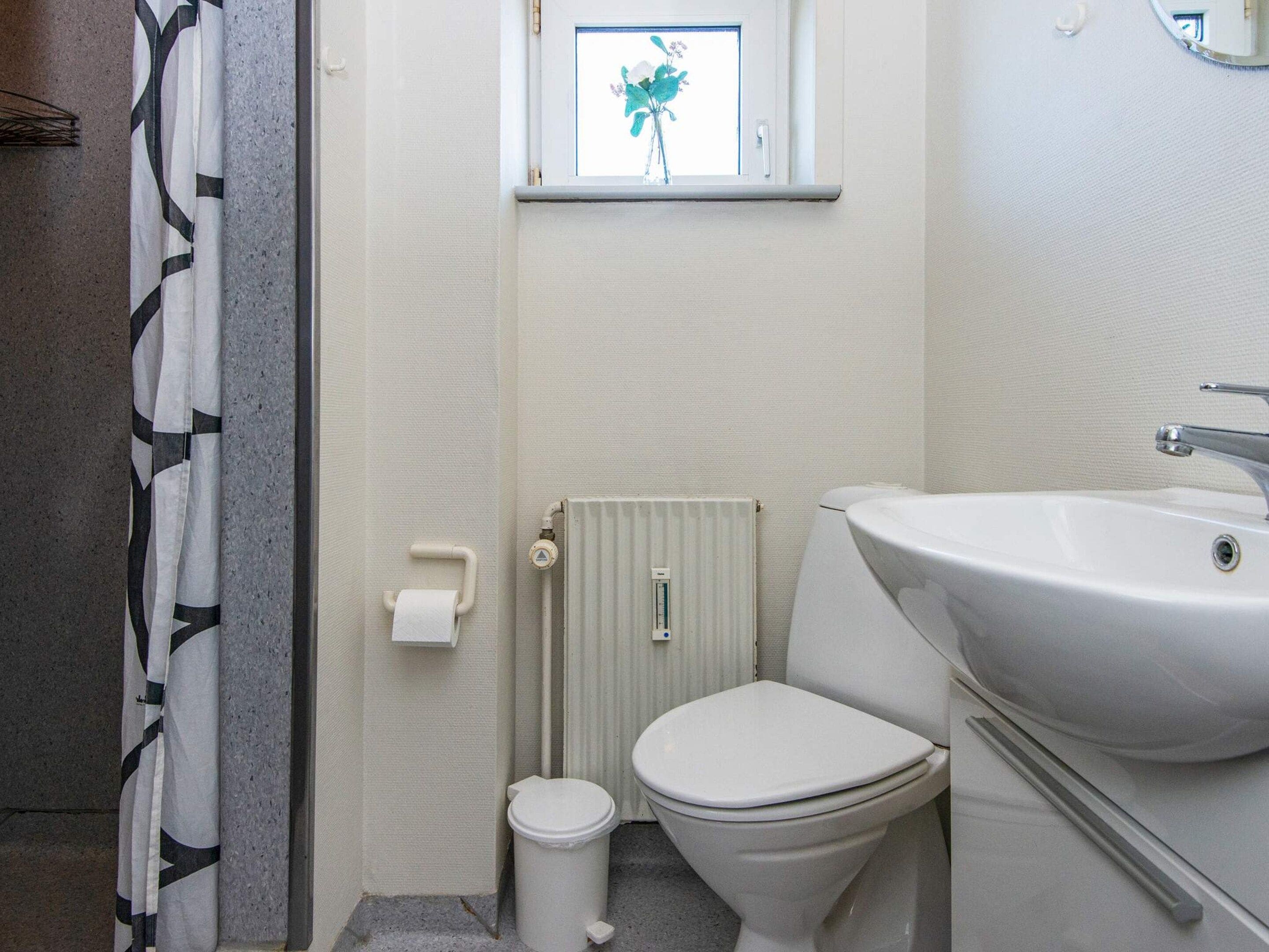 A bathroom with a toilet, a sink, a radiator, and a window with a plant.