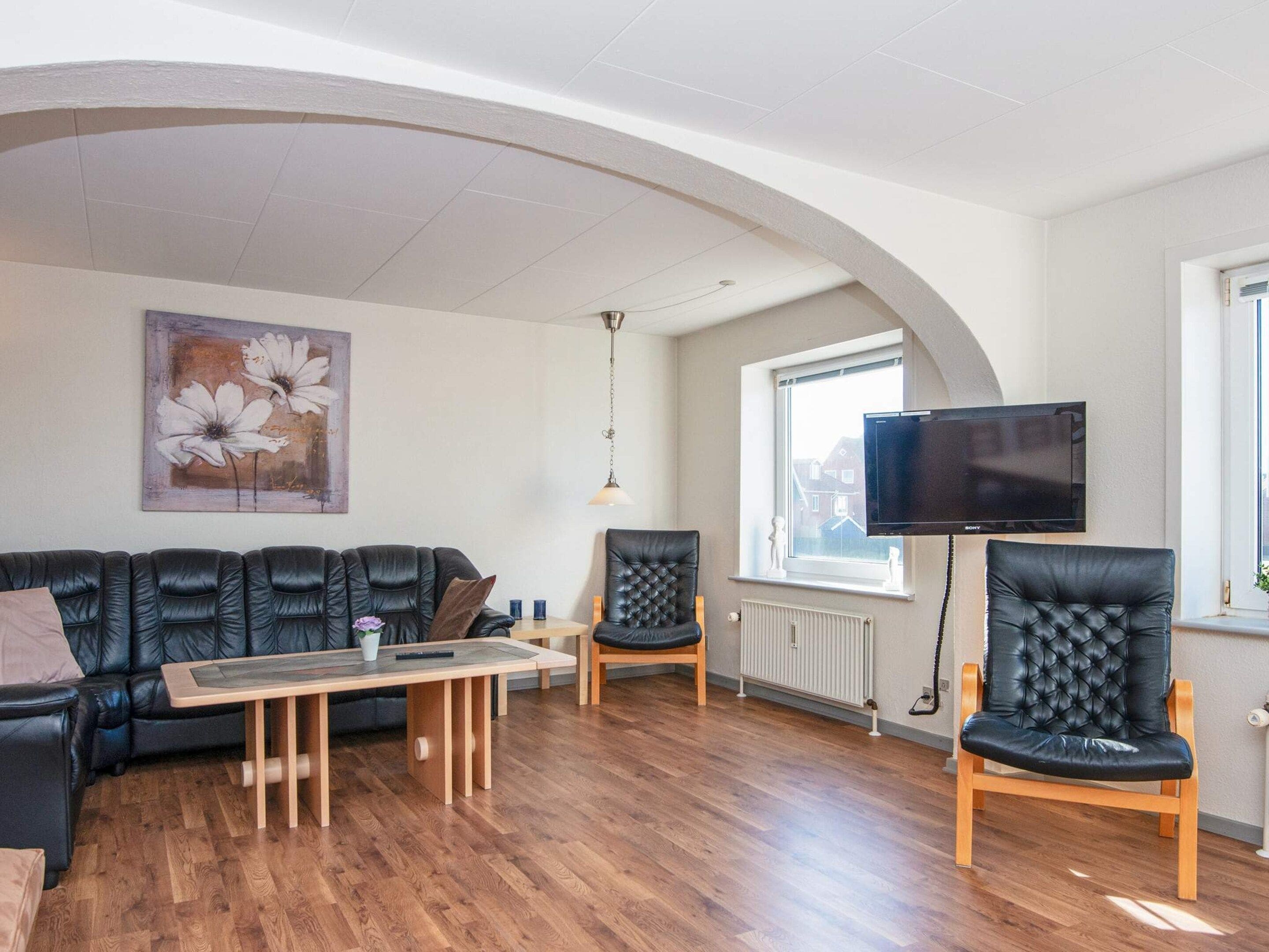 Un salon comprenant un canapé, des fauteuils, une table basse, un téléviseur à écran plat et un tableau accroché au mur.