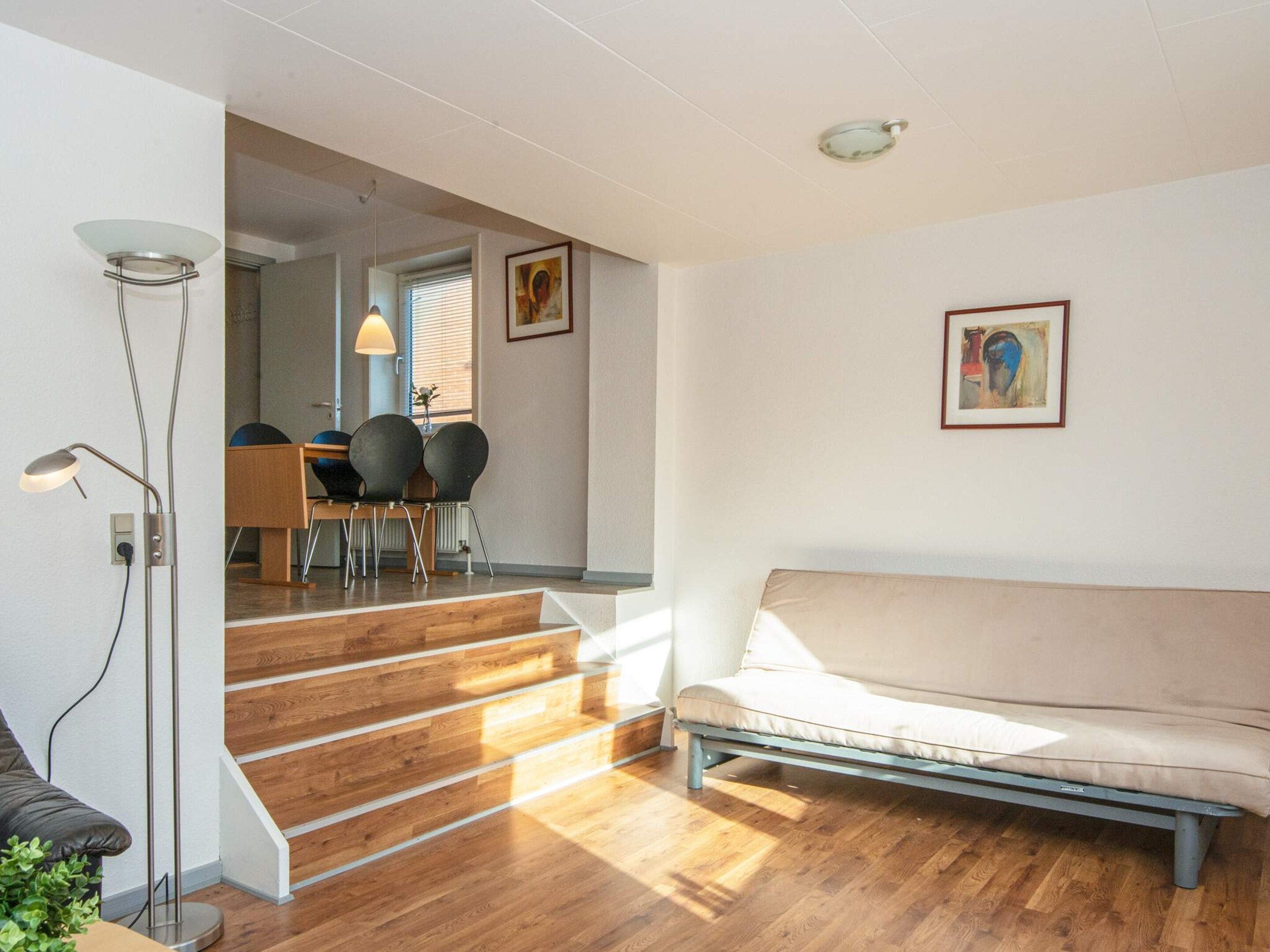 Uma sala de estar moderna com um sofá, uma área de jantar com cadeiras e uma escada que dá para outro quarto.