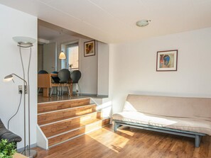 A modern living room with a sofa, a dining area with chairs, and a staircase leading to another room. - Smart Apartment in Thyborøn near Sea (Thyborøn)