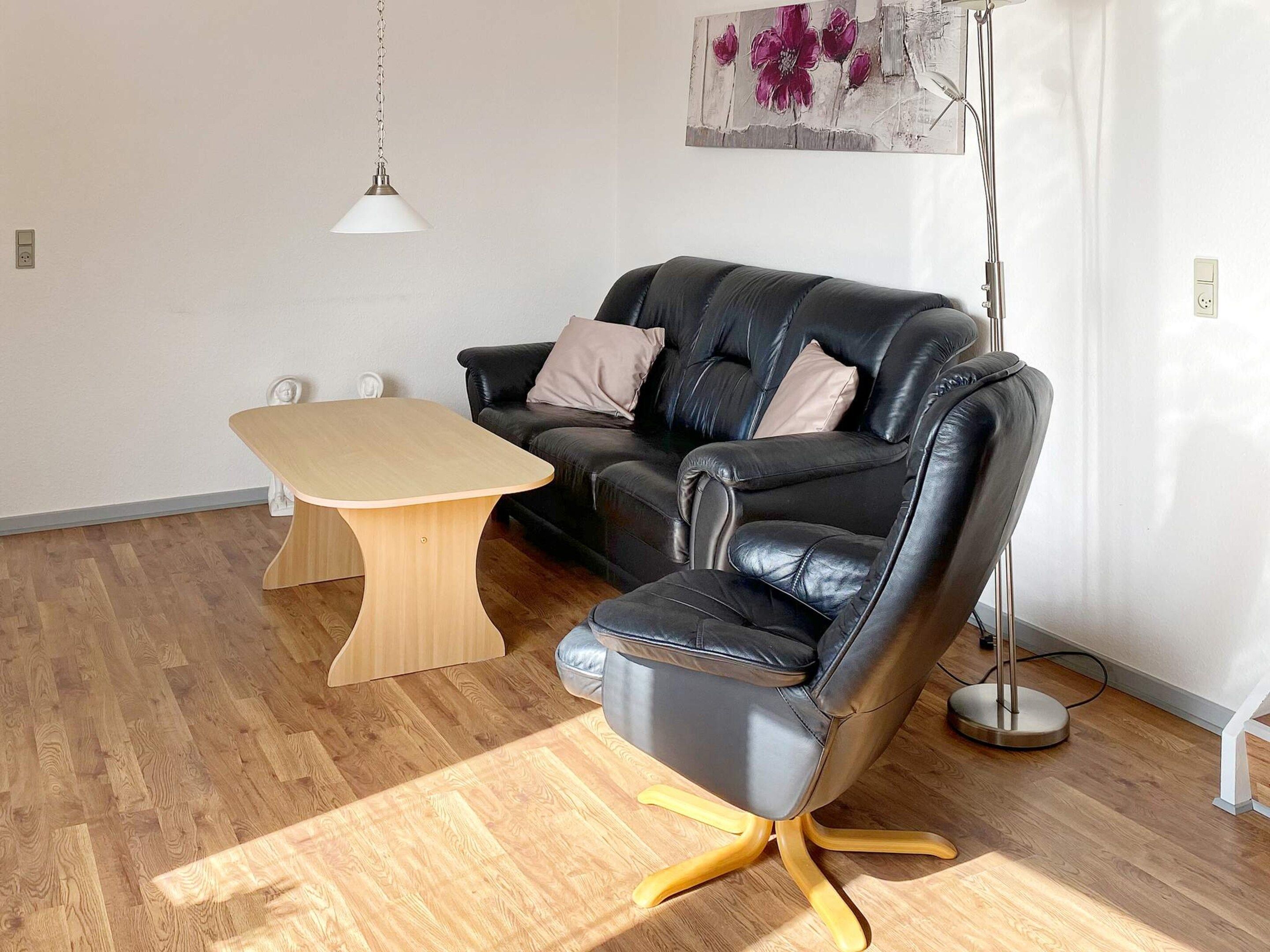 Una sala de estar moderna con un sofá de cuero negro, una mesa de centro de madera y una lámpara de pie.