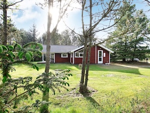 A red building with a white door and windows, surrounded by grass and trees.