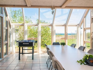 A room with a table and chairs, a foosball table, and large windows offering a view of the outdoors. - 4 Star Holiday Home in Haderslev (Haderslev)