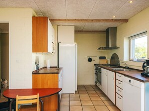 A compact kitchen with a dining table, wooden cabinets, a built-in oven, and a window providing natural light.