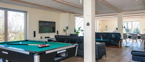 A spacious indoor area with a pool table, comfortable seating, and large windows.