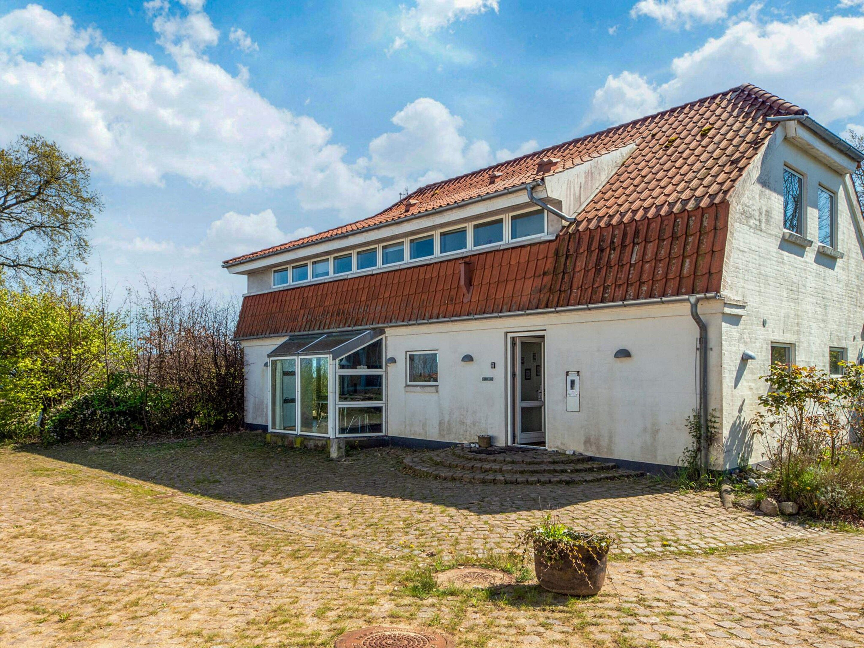 A two-story house with a red-tiled roof, a glass door entrance, and a paved courtyard.
