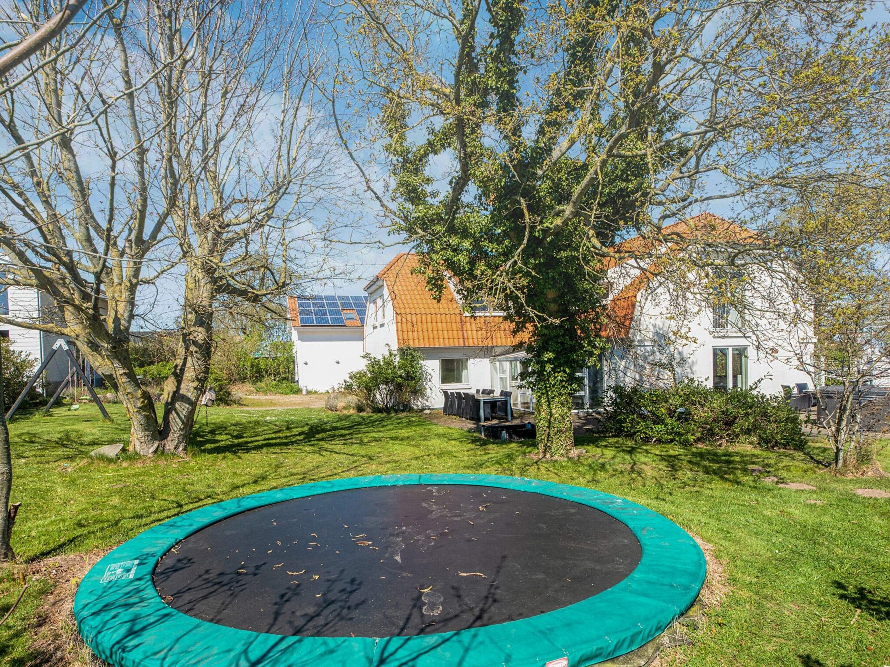 Ein Wohngebiet mit einem Trampolin im Vordergrund, umgeben von Bäumen und einem Haus mit einem Ziegeldach im Hintergrund.